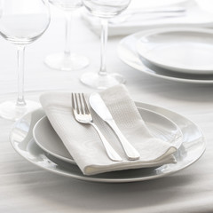 Table setting white and grey colour. Empty glasses and plates set with napkin and cutlery. Restaurant interior background...
