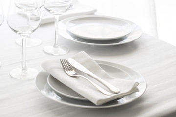 Table setting white and grey colour. Empty glasses and plates set with napkin and cutlery. Restaurant interior background...