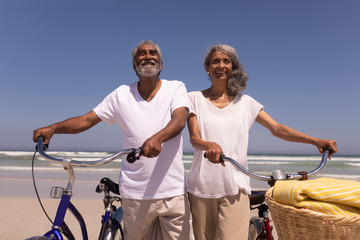 Senior couple walking with bicycle and looking each other on beach