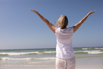 Rear view of senior woman standing with arms outstretched at beach 