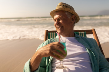 Senior man having cocktail drink while relaxing on sun lounger at beach