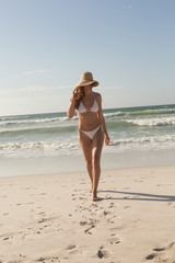 Fototapeta na wymiar Young Caucasian woman in hat and bikini walking on the beach