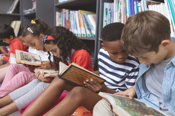 School kids sitting on cushions and studying over books in a library 