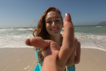 Young Caucasian woman hand reaching towards the camera at beach