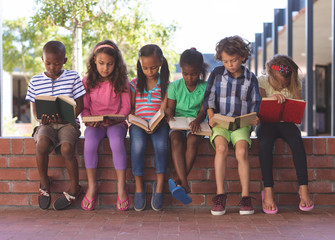 Students reading book while sitting on brick wall at corridor
