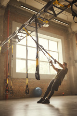 Strong athletic man training his arms with trx fitness straps at gym