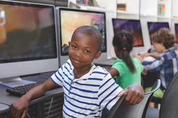 Happy schoolboy sitting in computer room 