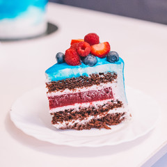 Close-up of a piece of festive blue and white cake decorated with fruits: strawberries, raspberries, blueberries. Cake for birthday, holiday and anniversary. Cake slice with filling