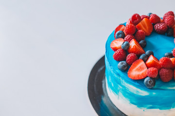 Close-up festive blue and white cake decorated with fruits: strawberries, raspberries, blueberries. Cake for birthday, holiday and anniversary. Space for text