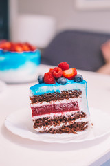 Close-up of a piece of festive blue and white cake decorated with fruits: strawberries, raspberries, blueberries. Cake for birthday, holiday and anniversary. Cake slice with filling