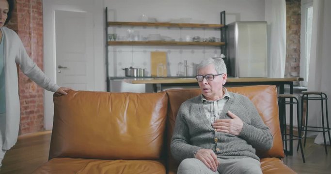 Senior woman comes to her husband suffering from heart disease and brings him glass of water