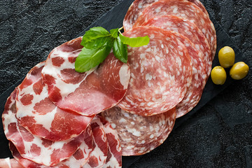 Italian meat snacks on a black slate board. Prosciutto Crudo, Milano Salami and Coppa Ham. Italian...