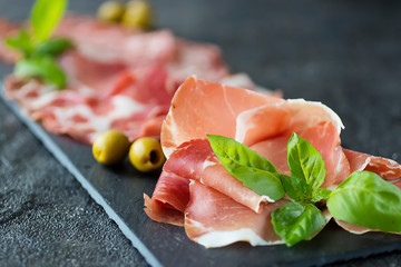 Italian meat snacks on a black slate board. Prosciutto Crudo, Milano Salami and Coppa Ham. Italian food.