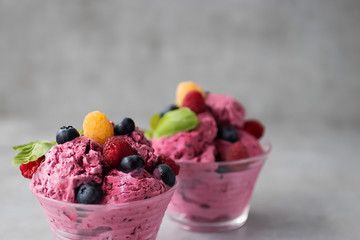 Homemade ice cream made from fresh berries with basil in glass bowl on a gray background.