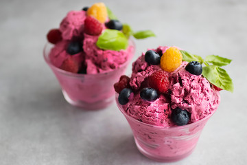 Homemade ice cream made from fresh berries with basil in glass bowl on a gray background.