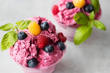 Homemade ice cream made from fresh berries with basil in glass bowl on a gray background.