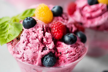 Homemade ice cream made from fresh berries with basil in glass bowl on a gray background.