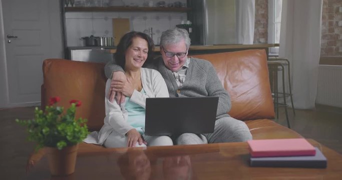 Smiling senior couple looks at laptop screen and chooses goods while shopping online at home
