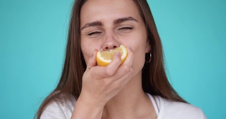 Young girl eats a lemon. Portrait of a beautiful woman. Girl grimaces while eating a sour lemon. Slow motion. Turquoise background.