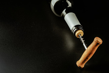 Bottle of wine and corkscrew over dark background