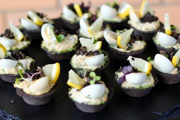 Tartlets with salmon , cream, olives, egg, herbs and a slice of lemon on a black background. Delicious snack. Concept of food, restaurant. Snack-antipasto. Selective focus.