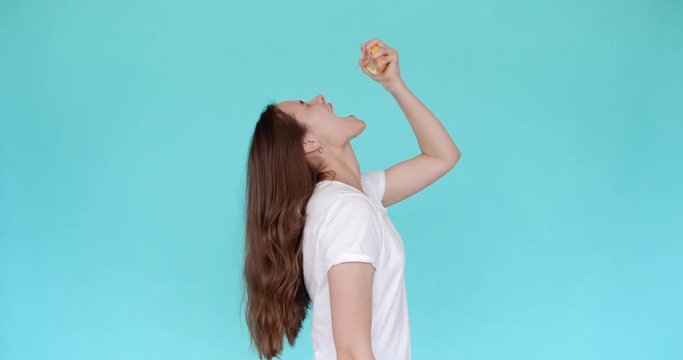 Beautiful girl squeezes lemon juice in her mouth. Slow motion. Turquoise background.
