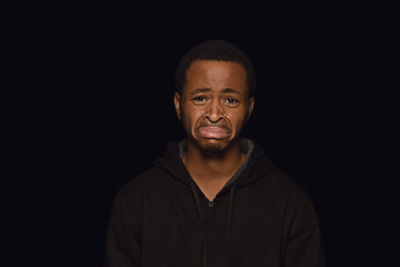 Close up portrait of young african-american man isolated on black studio background. Real emotions of male model. Crying and looks sad, upset. Facial expression, human nature and emotions concept.