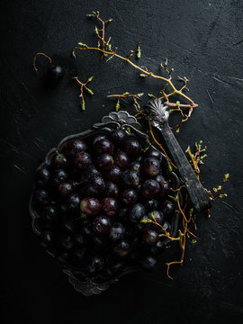 Grapes in a bowl on dark background with a vintage cutlery picker