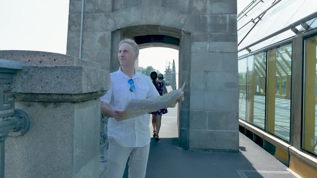 A man in a white shirt stands on a bridge and looks at a paper map of the city
