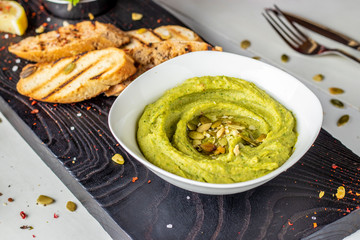 Hummus with spinach and pumpkin seeds in a bowl on a wooden board and bruschetta, oriental cuisine, horizontal photo