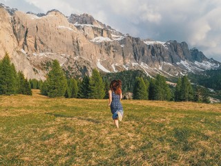 Naklejka premium Brunette girl with long hair in a dress on the floor running on the lawn overlooking the mountains in the sunset rays.