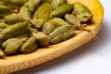 green cardamom on wooden spoon. white background. Close-up photo.