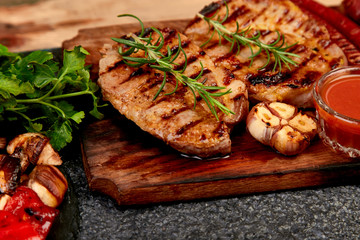 Grilled meat.  Steak pork grill on wooden cutting board with a variety of grilled vegetables on  black background. Copy space.