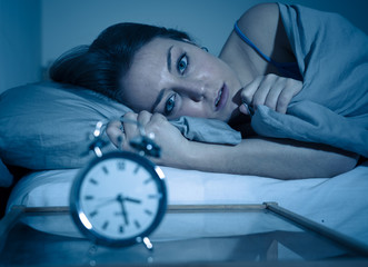 Attractive woman in bed staring at alarm clock trying to sleep feeling stressed and sleepless