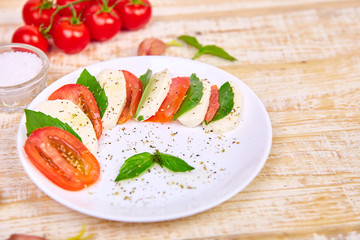Italian caprese salad with sliced tomatoes, mozzarella cheese, basil, olive oil on wooden background. Top view with space for your text