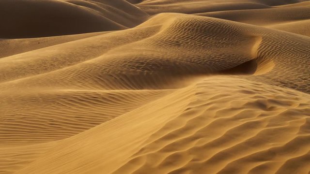 Sunset in desert. Sand is waving in the wind in sandy dunes in a desert. The dunes are covered with folds. UHD