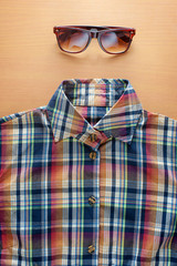 Shirt and sunglasses on wooden background.