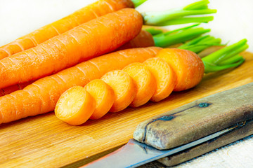 Fresh sliced carrots with green petiole on a wooden cutting board with knife. Raw carrots full of...