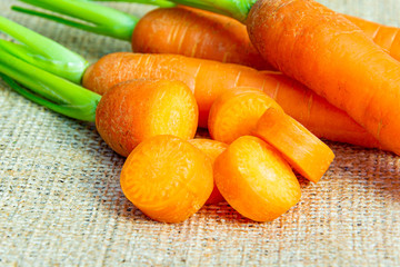 Fresh sliced carrots with green petiole on a jute background. Raw carrots full of vitamins ready...