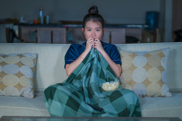  young beautiful scared and frightened Asian Chinese woman watching horror scary movie or thriller...