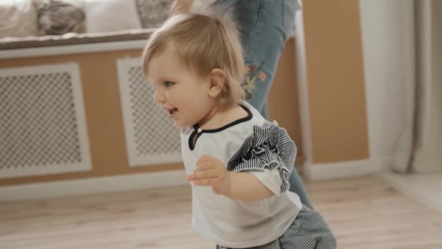 Close up view of small baby daughter walks holding her mom's hand indoor bootlessly slow motion