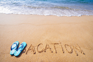 Traveling concept on the beach. Word Vacation written on the sand near the sea.