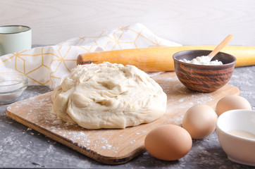 Prepared pizza dough on the wooden board. Ingredients for praparation of great homemade dough.Cup of milk,eggs,flour, rolling pin on the grey kitchen table
