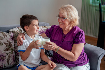 Beautiful grandmother and grandson are drinking milk and smiling while spending time together at...