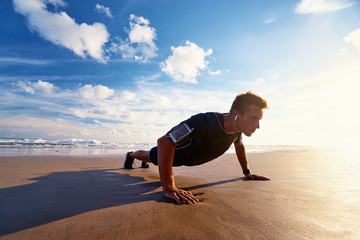 Sports and healthy lifestyle. Young man doing push-ups on the ocean beach.