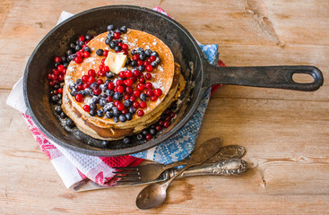 Homemade pancakes on a black cast iron skillet with berries on wooden background vintage tableware