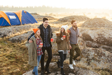 Group of friends outside in free alternative vacation camping over mountains drinking hot tea talking with each other.