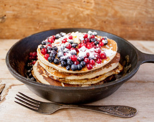 Homemade pancakes on a black cast iron skillet with berries on wooden background vintage tableware