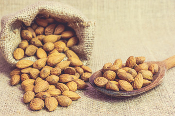 Ripe unpeeled almonds in jute bag and on wooden spoon on jute background