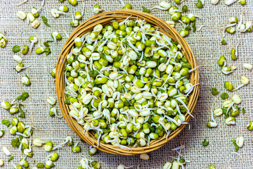 Flat lay photo of green fresh mungo sprouts in a wicker bowl on a wooden background. Food...